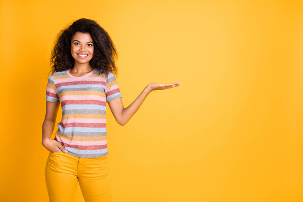 Portrait of her she nice attractive cheerful cheery content wavy-haired girl wearing striped tshirt holding in palm invisible object ad isolated on bright vivid shine vibrant yellow color background - Foto, afbeelding