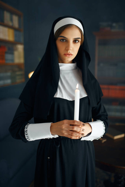 A freira jovem em uma batina mantém uma vela. A irmã está se preparando para a oração no mosteiro, religião e fé, pessoas religiosas
 - Foto, Imagem