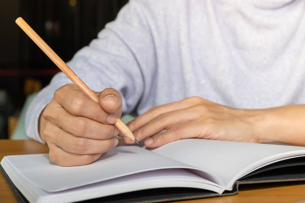 Close-up of woman writing  on blank empty paper notebook with wood pencil on wooden table in office - Foto, afbeelding