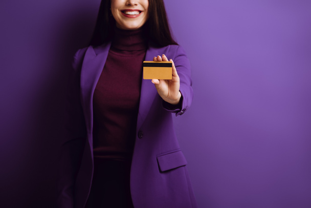 vista recortada de la mujer sonriente que muestra la tarjeta de crédito sobre fondo púrpura
 - Foto, Imagen