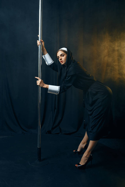 Sexy nun in a cassock dances on a pole like a stripper, vicious desires. Corrupt sister in the monastery, sinful religious people, attractive sinner - Photo, Image