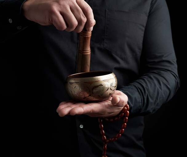 дорослий чоловік в чорній сорочці обертає дерев'яну паличку навколо копа
 - Фото, зображення