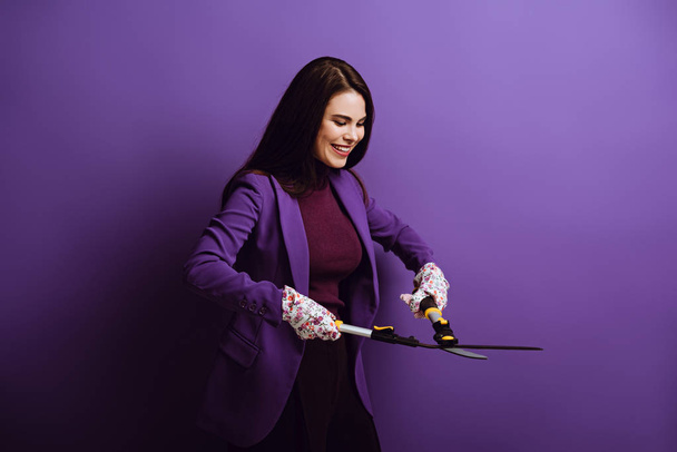 紫色の背景にガーデニングはさみを持って働く手袋の笑顔の女性 - 写真・画像