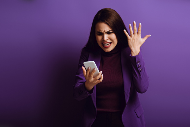 mujer joven enojada de pie con la mano levantada mientras tiene video chat sobre fondo púrpura
 - Foto, imagen
