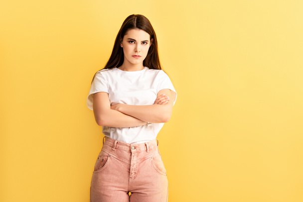 offended girl standing with crossed arms and looking at camera isolated on yellow - Foto, afbeelding