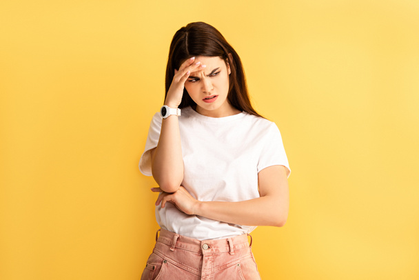 tired, upset girl touching head while suffering from headache isolated on yellow - Foto, afbeelding