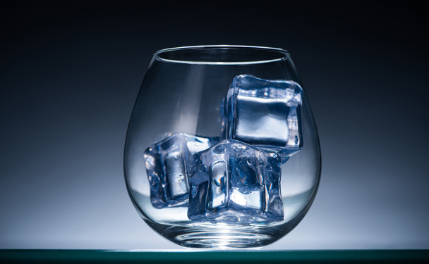 transparentes Glas mit Eiswürfeln in dunkel mit blauer Hintergrundbeleuchtung - Foto, Bild
