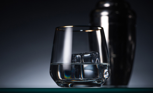 selective focus of transparent glass with ice cube and vodka in dark with back light and shaker - Foto, Bild