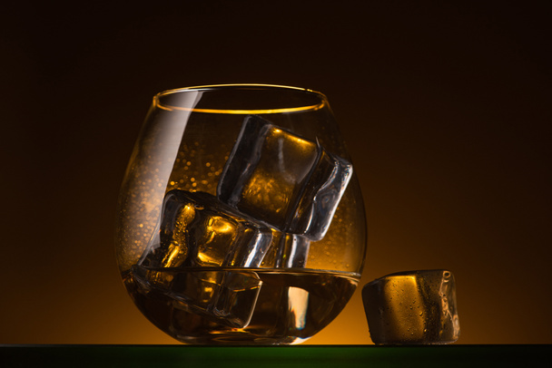 transparentes Glas mit Eiswürfeln und Wodka im Dunkeln mit warmem Gegenlicht - Foto, Bild