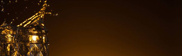 fedett üveg fröccsenő vodkával sötétben meleg hátfénnyel, panorámás felvétel - Fotó, kép