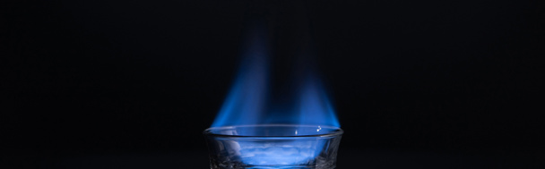 transparant glas met brandende vloeistof geïsoleerd op zwart, panoramisch schot - Foto, afbeelding