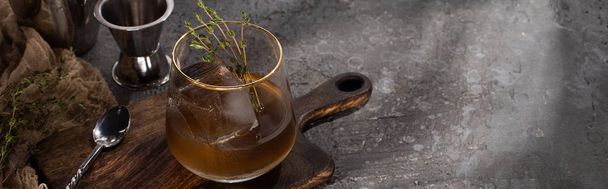 transparent glass with herb, ice cube and whiskey on concrete surface with bar equipment, panoramic shot - Photo, Image