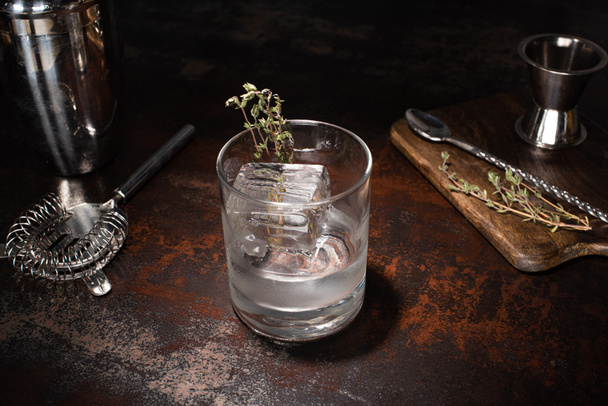 διαφανές γυαλί με βότανο, παγάκι και βότκα σε ξεπερασμένη επιφάνεια - Φωτογραφία, εικόνα