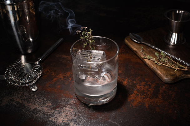 прозрачное стекло с горящей травой, кубиком льда и водкой на выветренной поверхности
 - Фото, изображение