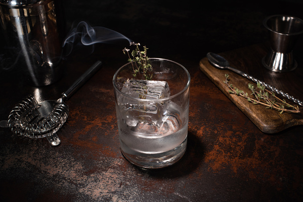 transparentes Glas mit brennendem Kraut, Eiswürfel und Wodka auf verwitterter Oberfläche - Foto, Bild