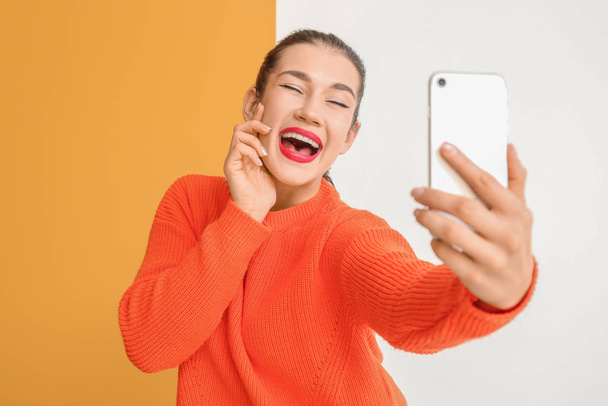 Schöne junge Frau macht Selfie auf farbigem Hintergrund - Foto, Bild