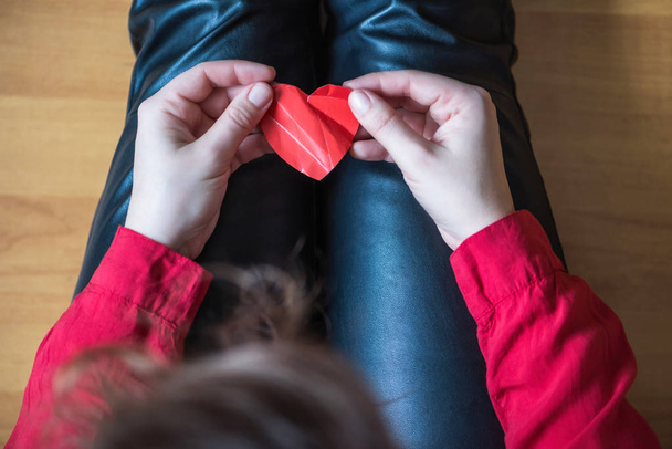 woman with crumpled paper heart in the hand sitting on the floor.  Broken relationships in bad Valentine's day. concept. Top view - Valokuva, kuva