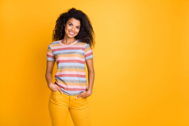 Portrait of her she nice attractive lovely cheerful cheery content wavy-haired girl wearing striped tshirt holding hands in pockets isolated over bright vivid shine vibrant yellow color background - Fotografie, Obrázek