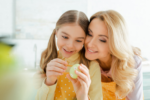 foco seletivo da mãe feliz perto da filha pintando ovo de Páscoa
  - Foto, Imagem