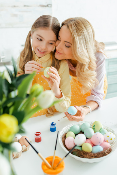 selective focus of happy mother near cute daughter painting easter egg  - Fotografie, Obrázek