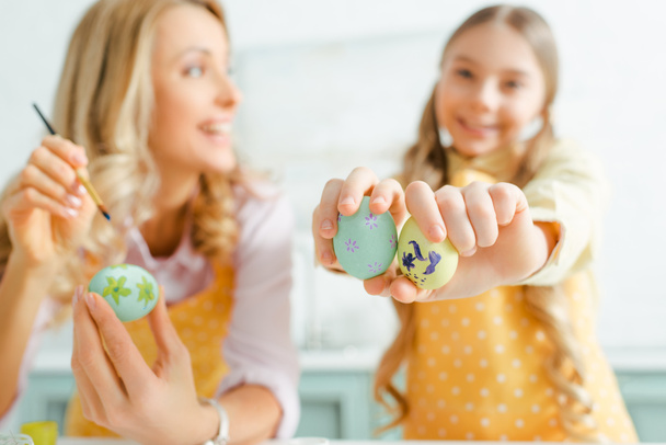 selective focus of happy kid holding painted easter eggs near mother  - 写真・画像