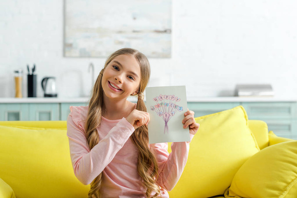 cheerful kid holding greeting card with happy mothers day lettering  - Fotoğraf, Görsel