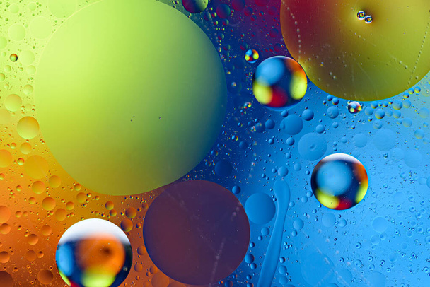 levendige bellen van oliedruppels op wateroppervlak op gekleurde achtergrond - Foto, afbeelding