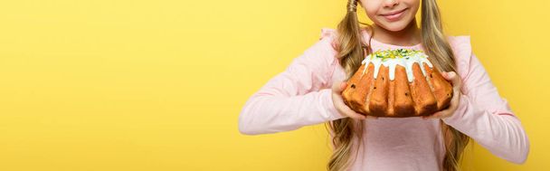 панорамный снимок счастливого ребенка, держащего пасхальный торт изолирован на желтый
  - Фото, изображение