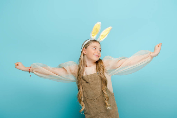 veselé dítě s králičí uši a natažené ruce izolované na modré  - Fotografie, Obrázek