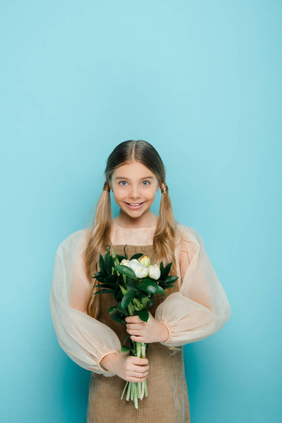 happy kid holding bouquet of flowers on blue  - Foto, immagini
