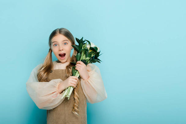 shocked kid holding bouquet of flowers on blue  - Zdjęcie, obraz