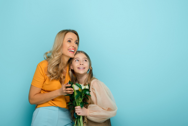 cheerful mother and daughter smiling near tulips isolated on blue - Φωτογραφία, εικόνα