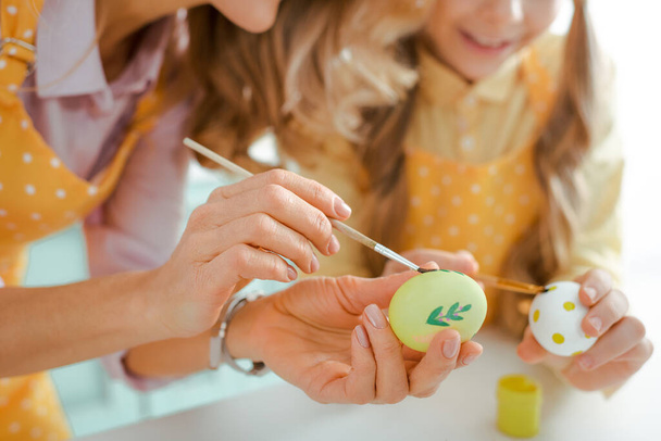 przycięty widok matki i córki malujących jaja kurze na Wielkanoc  - Zdjęcie, obraz