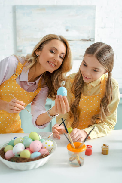 happy woman and adorable kid looking at painted chicken egg on easter  - Photo, Image