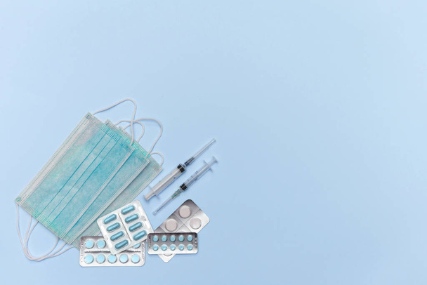 Medical masks, pills and syringes lie on a sky blue background top view. Recommendation of protection against coronavirus viruses and prevention and treatment of colds. - 写真・画像