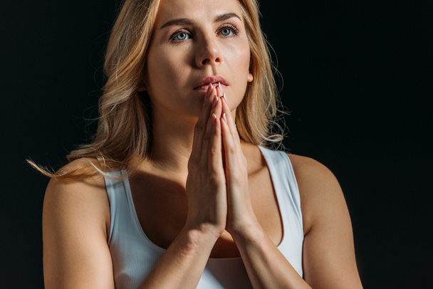 Woman with clenched hands praying isolated on black - Foto, Bild