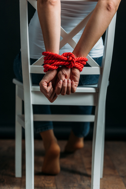 Cropped view of woman with tied hands on chair on black background - Foto, Imagem