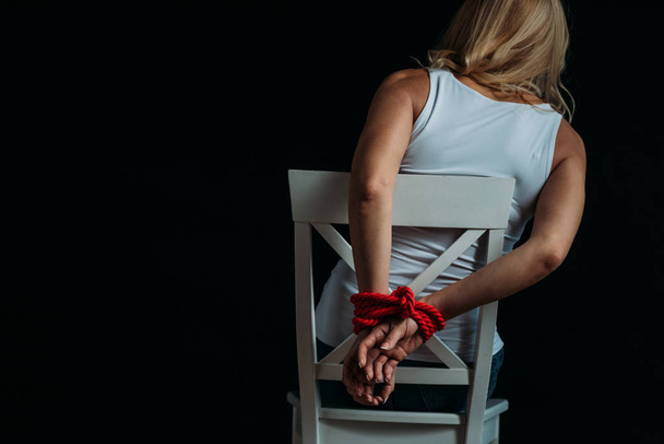 Back view of woman with tied hands sitting on white chair isolated on black - Fotoğraf, Görsel