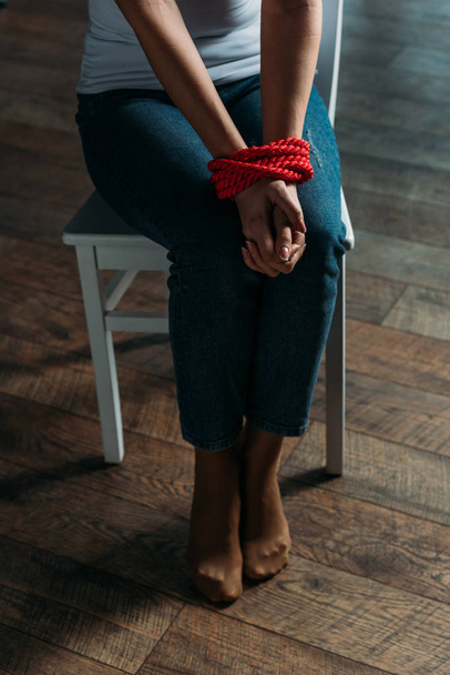 Cropped view of woman with tied hands sitting on chair on wooden background - Foto, afbeelding