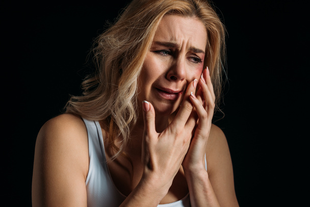 Žena pláče a dotýká tvář s modřinami izolované na černé  - Fotografie, Obrázek