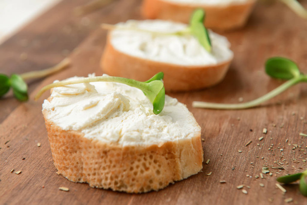 ломтики вкусного хлеба со сливочным сыром на деревянной доске, крупным планом
 - Фото, изображение