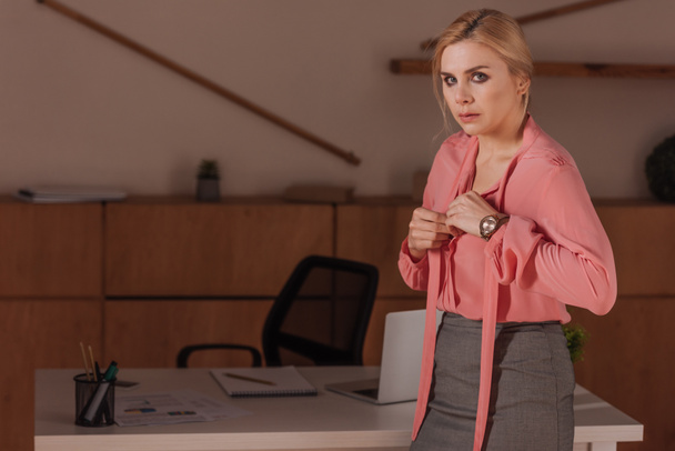 Focus selettivo della donna guardando la fotocamera e abbottonatura camicetta rosa in ufficio, concetto di molestie sessuali
 - Foto, immagini