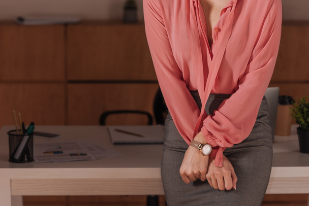 Oříznutý pohled na ženu se zaťatýma rukama u stolu v kanceláři, koncept sexuálního obtěžování - Fotografie, Obrázek