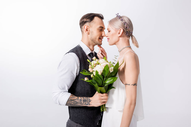 beautiful tattooed bride and handsome bridegroom standing nose to nose isolated on white - Foto, afbeelding