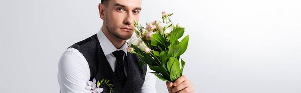 handsome tattooed elegant bridegroom with bouquet on grey, panoramic shot - Photo, Image