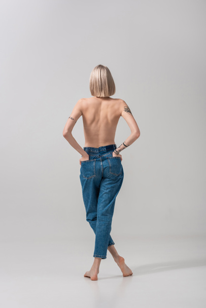 back view of sexy young topless tattooed woman with hands in pockets on grey - Foto, immagini
