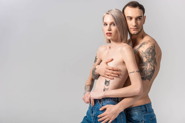 joven sin camisa tatuado pareja en jeans abrazo aislado en gris
 - Foto, Imagen