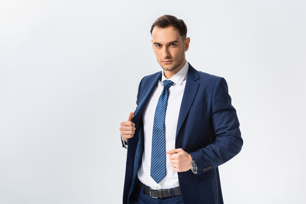 successful young businessman in blue suit with hands on blazer isolated on white - 写真・画像
