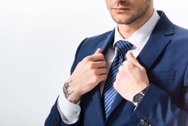 cropped view of successful tattooed businessman in blue suit with hands on blazer isolated on white - Fotoğraf, Görsel