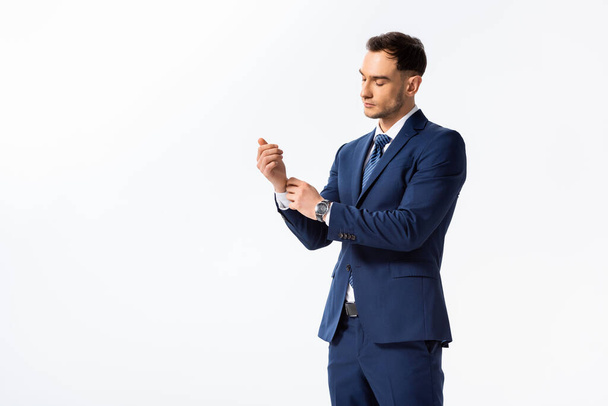 successful young businessman in blue suit adjusting shirt isolated on white - 写真・画像